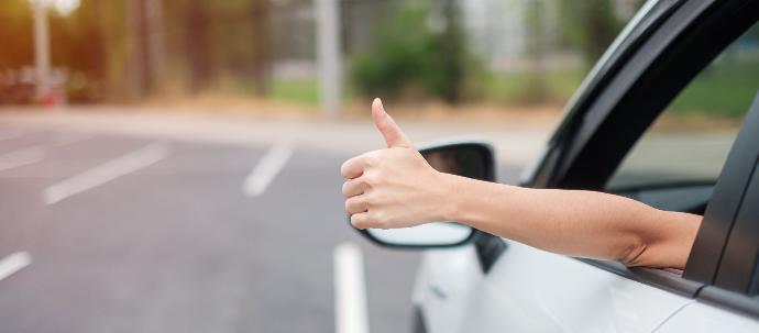 Conductora levantando el dedo de manera positiva por fuera de la ventana mientras está dentro del coche
