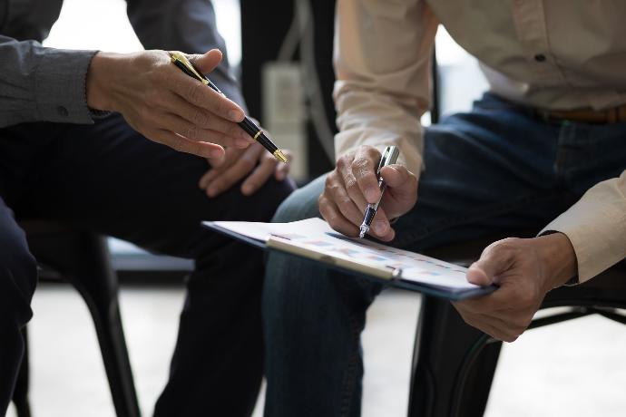 Personas debatiendo sobre la firma de documentos mientras ambos sujetan un bolígrafo