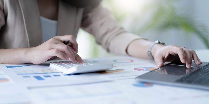 Informe gestión Mujer en ropa corporativa usando una calculadora y un ordenador portátil revisando unas cuentas o gráficos