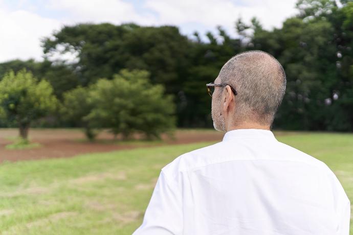 Hombre de espaldas contemplando terreno de césped y árboles